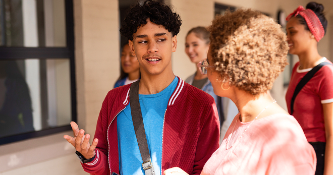 Teenage student speaking with a teacher outside a campus building.