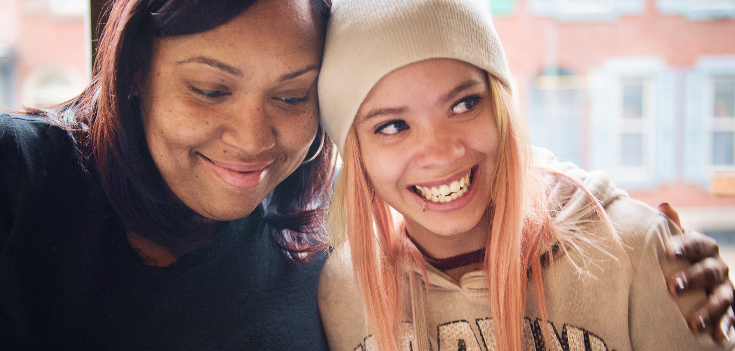 Mother and teenager smiling and standing with their heads close together.