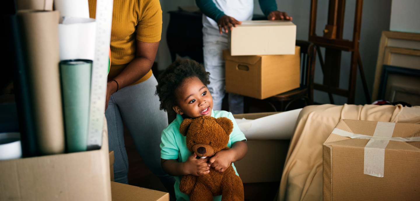 Child holding a teddy bear as his family unpacks boxes in their new house.
