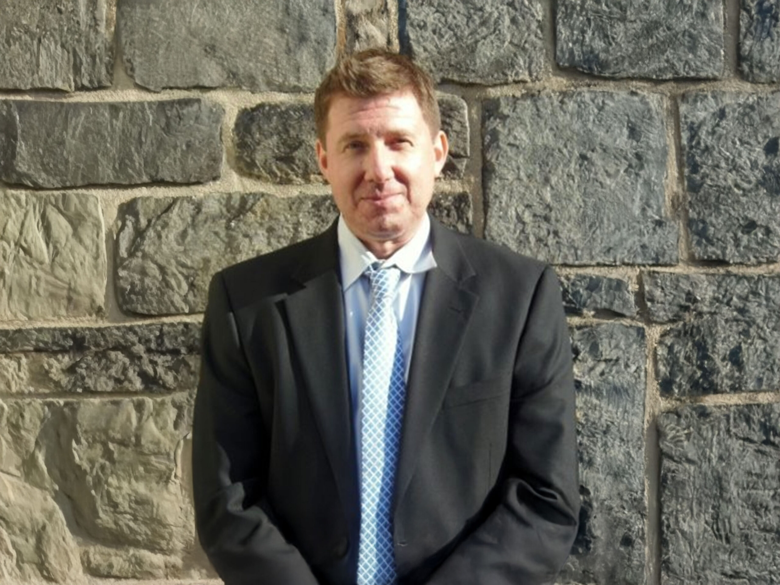 Ivan Haskell, Executive Director of the Joseph J. Peters Institute, standing outside in front of a gray brick wall