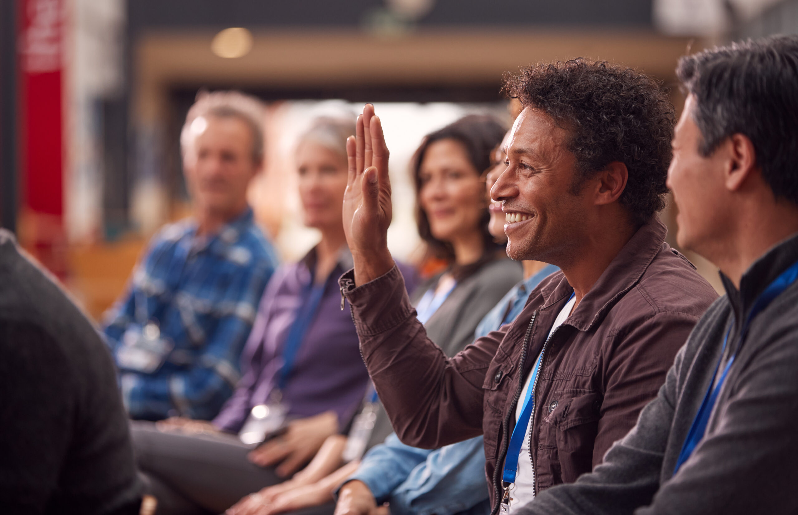 A man raising his hand to speak during a presentation at a conference breakout session.